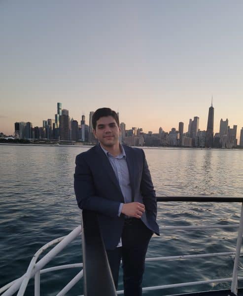 Gabriel Martinez stands on a boat on a river. City skyline in the background.