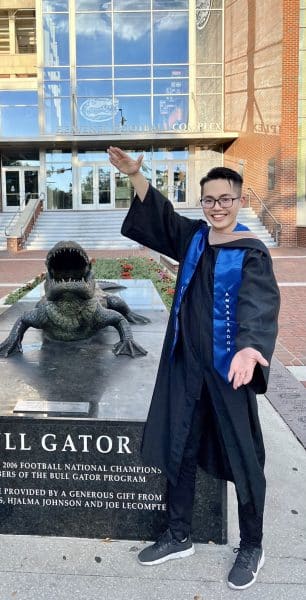 Chia Han Lin does the gator chomp in his graduation gown next to the statue of a gator.