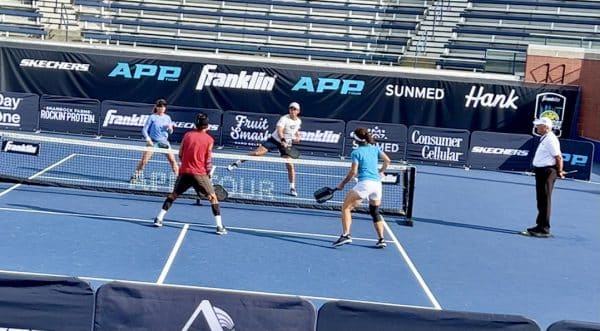 A group of four people playing pickleball on a court while a referee watches. 