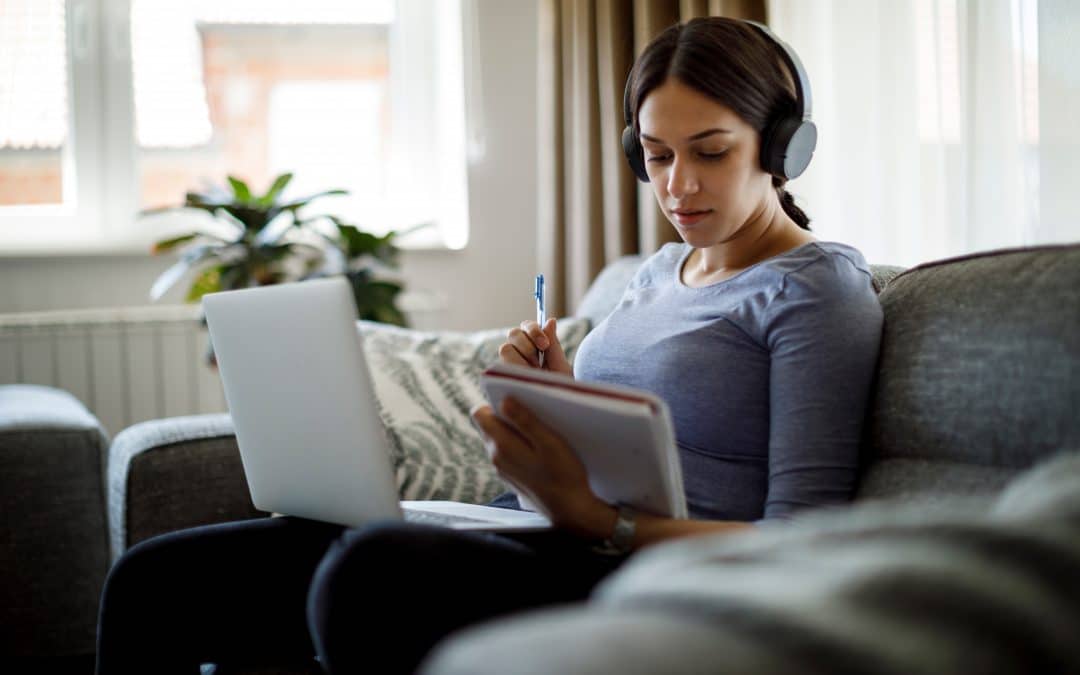 Serious young woman wearing headphones studying at home with a laptop computer