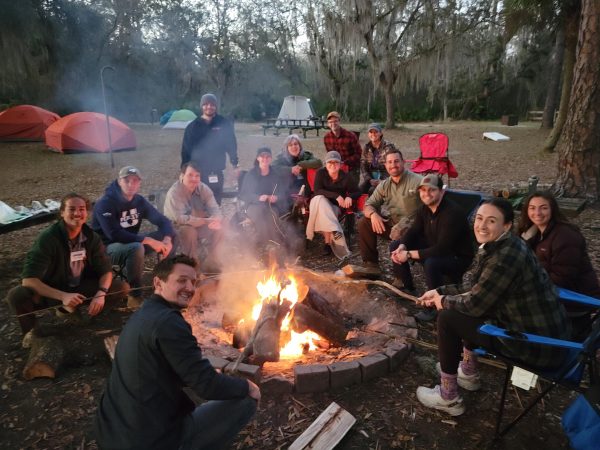 Students sit around a campfire.