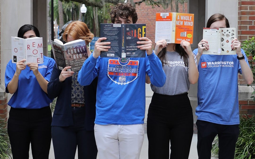 Five students stand in a v-formation holding books in front of their faces