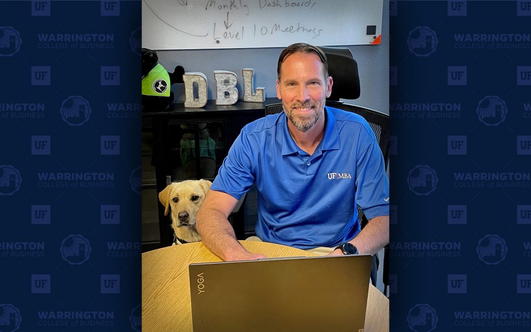 Bryan Williams sits at a desk with a dog sitting beside him.