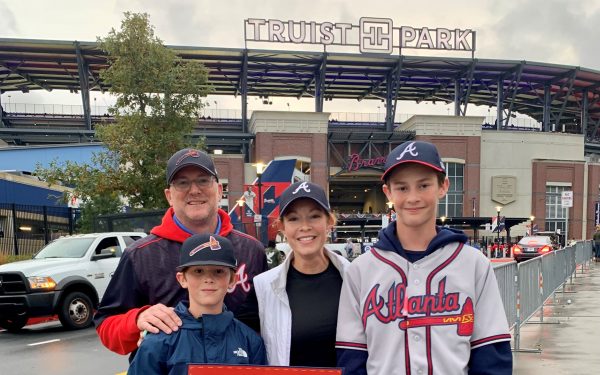 A family of 4 wearing Atlanta Braves attire pose for a photo in front of Truist Park.