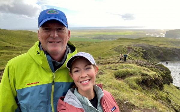 A man and a woman pose for a selfie on a cliff while hiking.