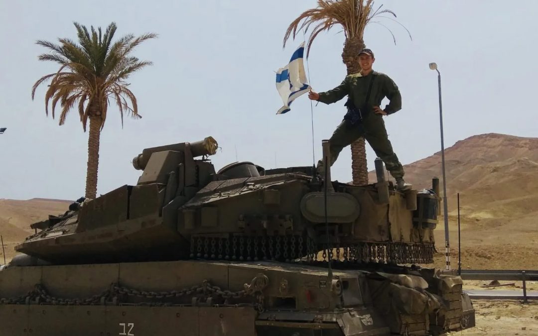 Alexander Schwartz standing on top of a tank holding the Israeli flag.