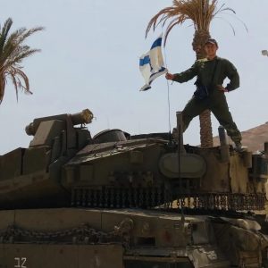 Alexander Schwartz standing on top of a tank holding the Israeli flag.