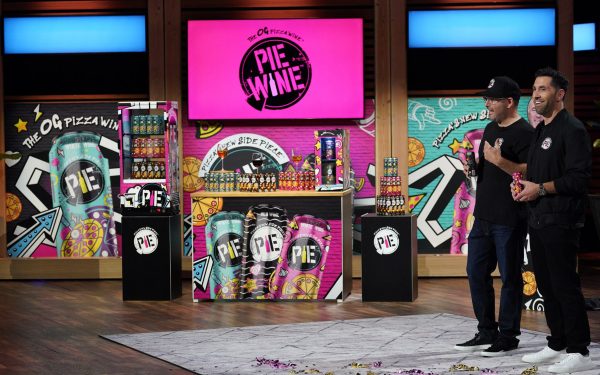 Joshua Green and his business parter pose in front of a colorful background on the TV show, Shark Tank.