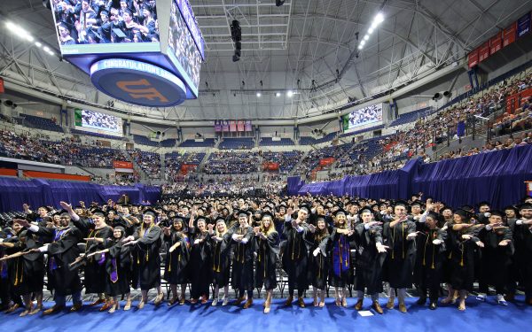 A large arena with students in rows standing while doing the Gator chomp.
