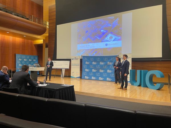 Students present a powerpoint presentation on a stage to a panel of judges.