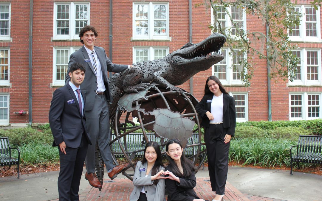 Five students pose around a statue of an alligator.