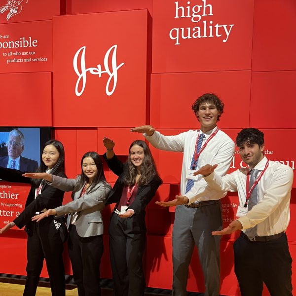 Five students doing the Gator chomp in front of Johnson & Johnson's logo.