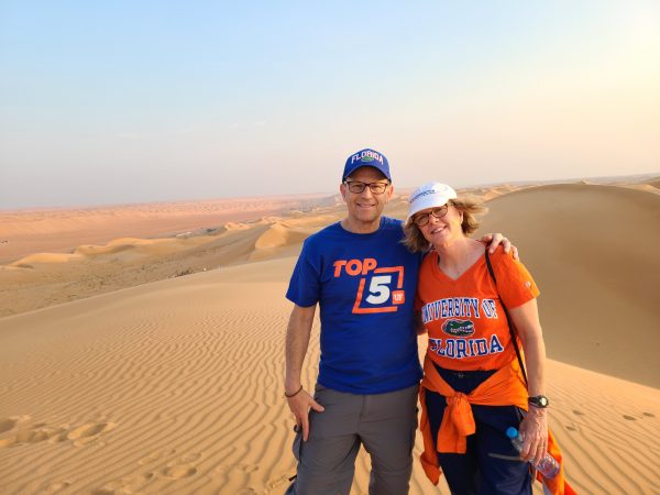 Bill and Carol Moss wearing University of Florida shirts in front of a desert background in Oman