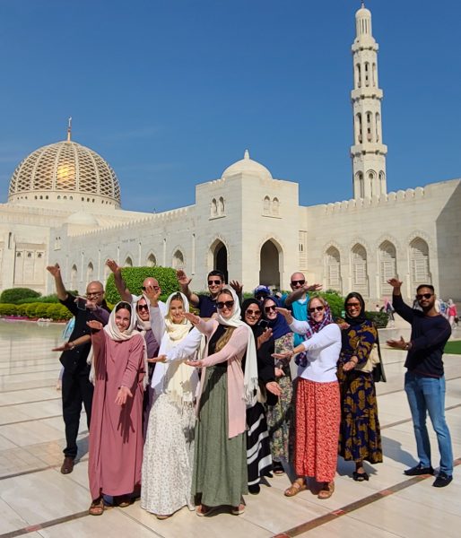 A group of students pose in front of a mosque in Oman while doing the Gator Chomp.