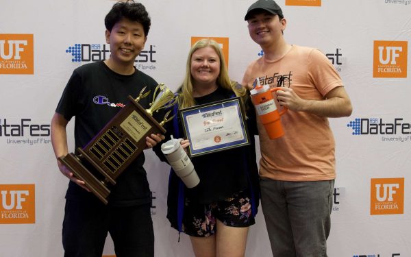 Three students pose for a photo with a large trophy and certificate for winning at DataFest.