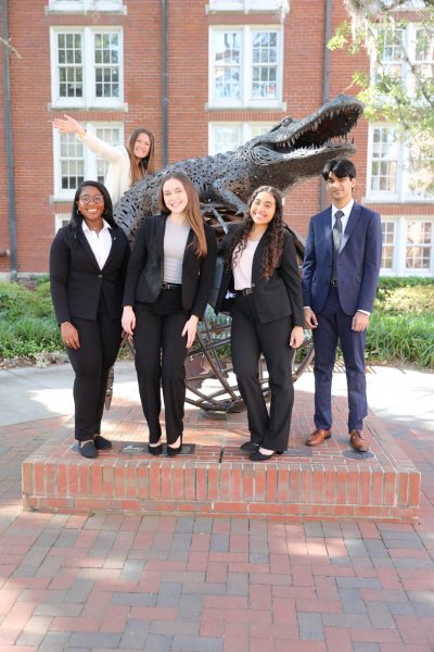 Five students pose on and around a gator statue.
