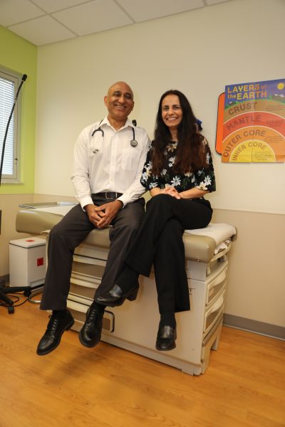 Sanjeev Tuli and Sonal Tuli sit on a patient table in a pediatrics exam room.
