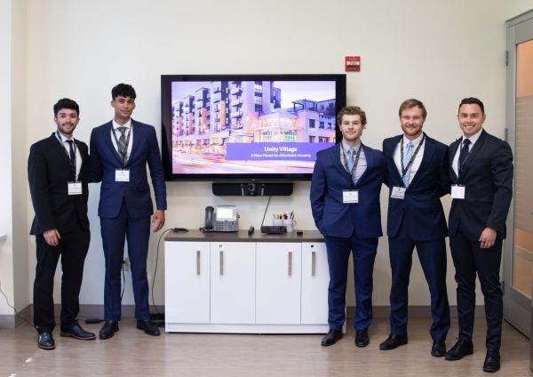 Students pose next to a screen displaying a digital real estate model.