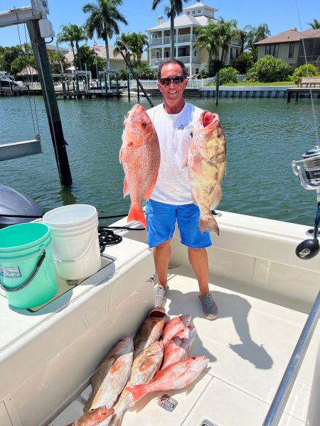 Greg Rosica holding two fish on a boat.