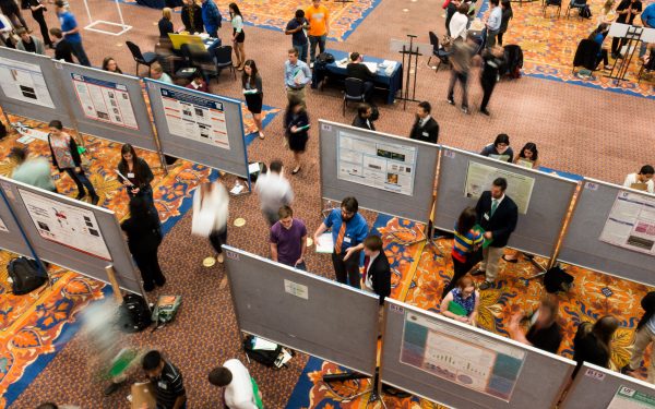 Birds eye view of an undergraduate research event. Large room with student research project posters and people walking around looking at the poster content.