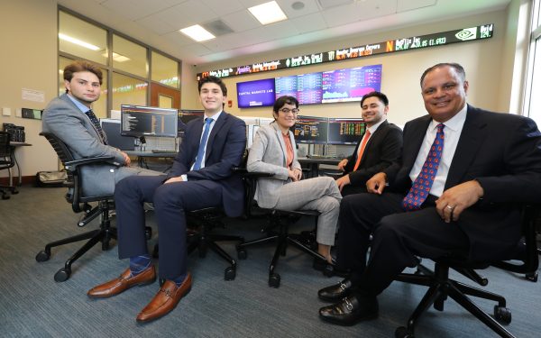 Four students and Eddie Sanchez sit in front of Bloomberg terminals.