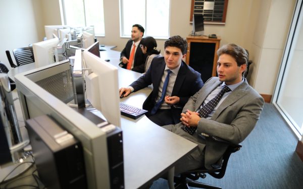 Two students face a Bloomberg Terminal while discussing information on the screen.