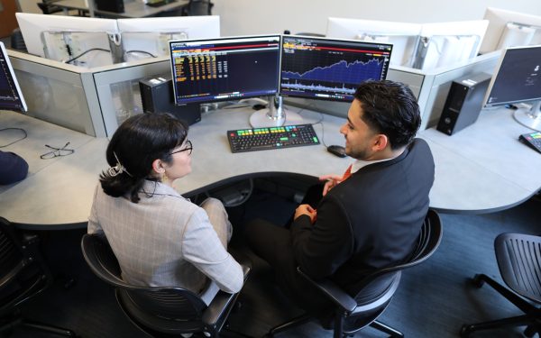 Birds-eye view of two students sitting in front of a Bloomberg Terminal discussing the information on the screen.