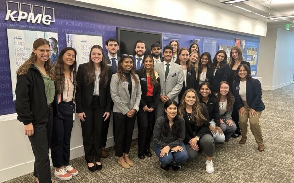 About 20 students pose for a photo in front of the KPMG logo in the company's office.