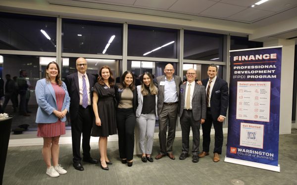 8 people pose for a photo next to a large rollup banner detailing the Finance Professional Development program