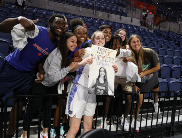 Basketball player Paige Clausen holds up a poster while surrounded by her friends in the stands.