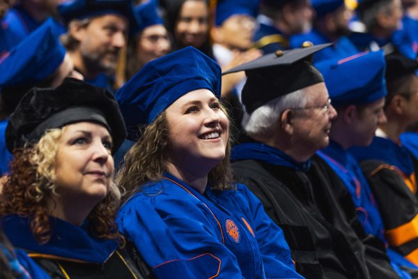 A doctoral candidate in graduation regalia smiles amongst her peers.