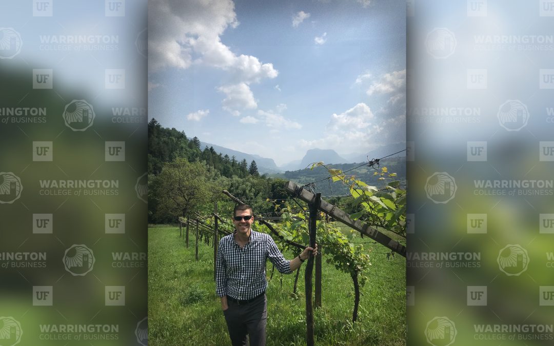 Rob Cornella stands in a lush vineyard surrounded by mountains.