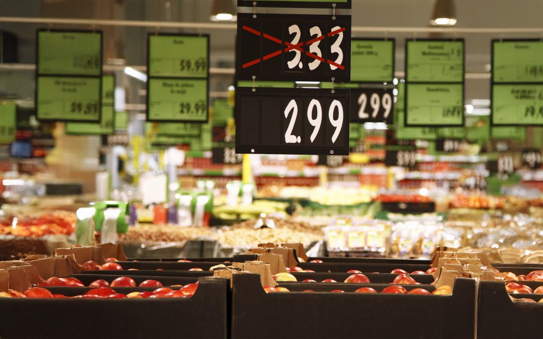 Grocery store price signs hang from ceiling above produce indicating price drop from $3.33 to $2.99.