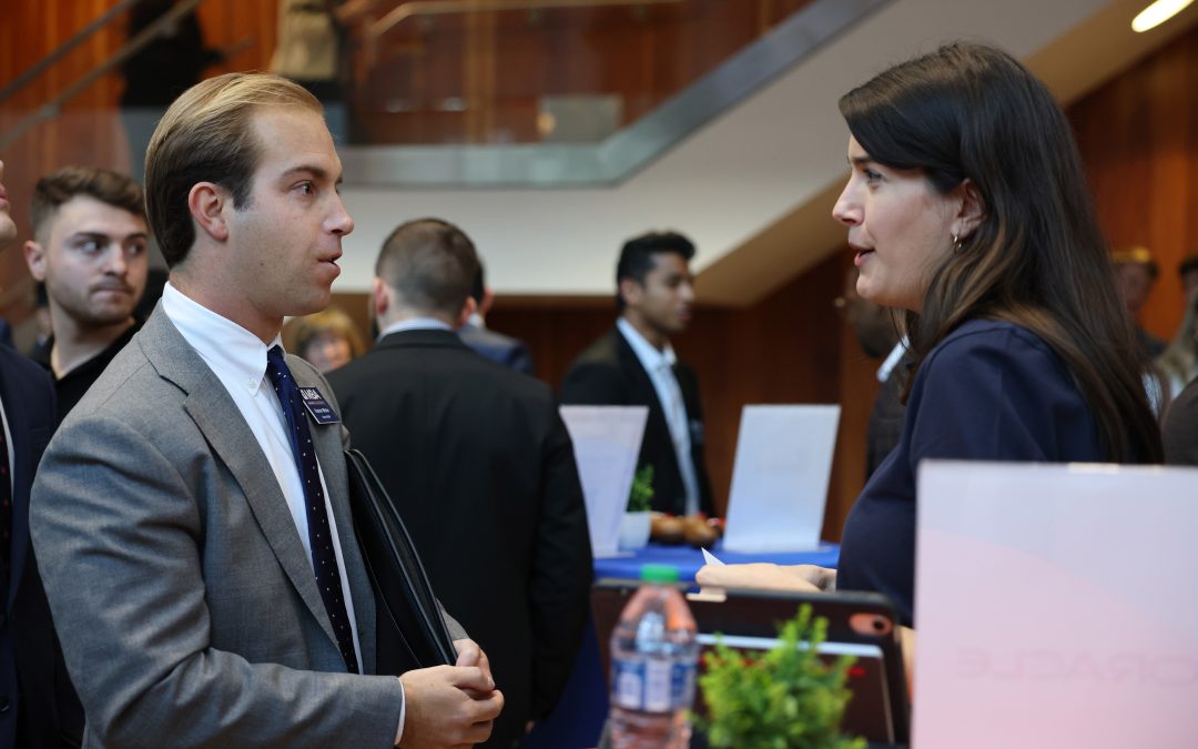 An MBA student wearing a suit speaks with another person in a suit while at a networking event.