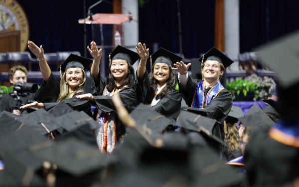 Four 2023-2024 Graduate students do the Gator Chomp wearing their cap and gown at the 2023-2024 Commencement Ceremony.