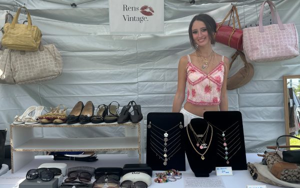 Lauren Kurtz smiling at a white booth, reselling luxury goods for her business Rens Vintage at a vintage market.