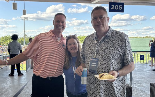 Three people wearing Gator gear pose for a photo at a baseball game during DBA Alumni Weekend.