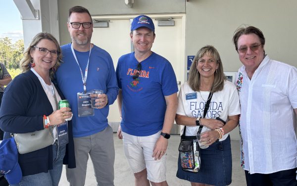 Five people wearing orange and blue post for a photo during a baseball game.